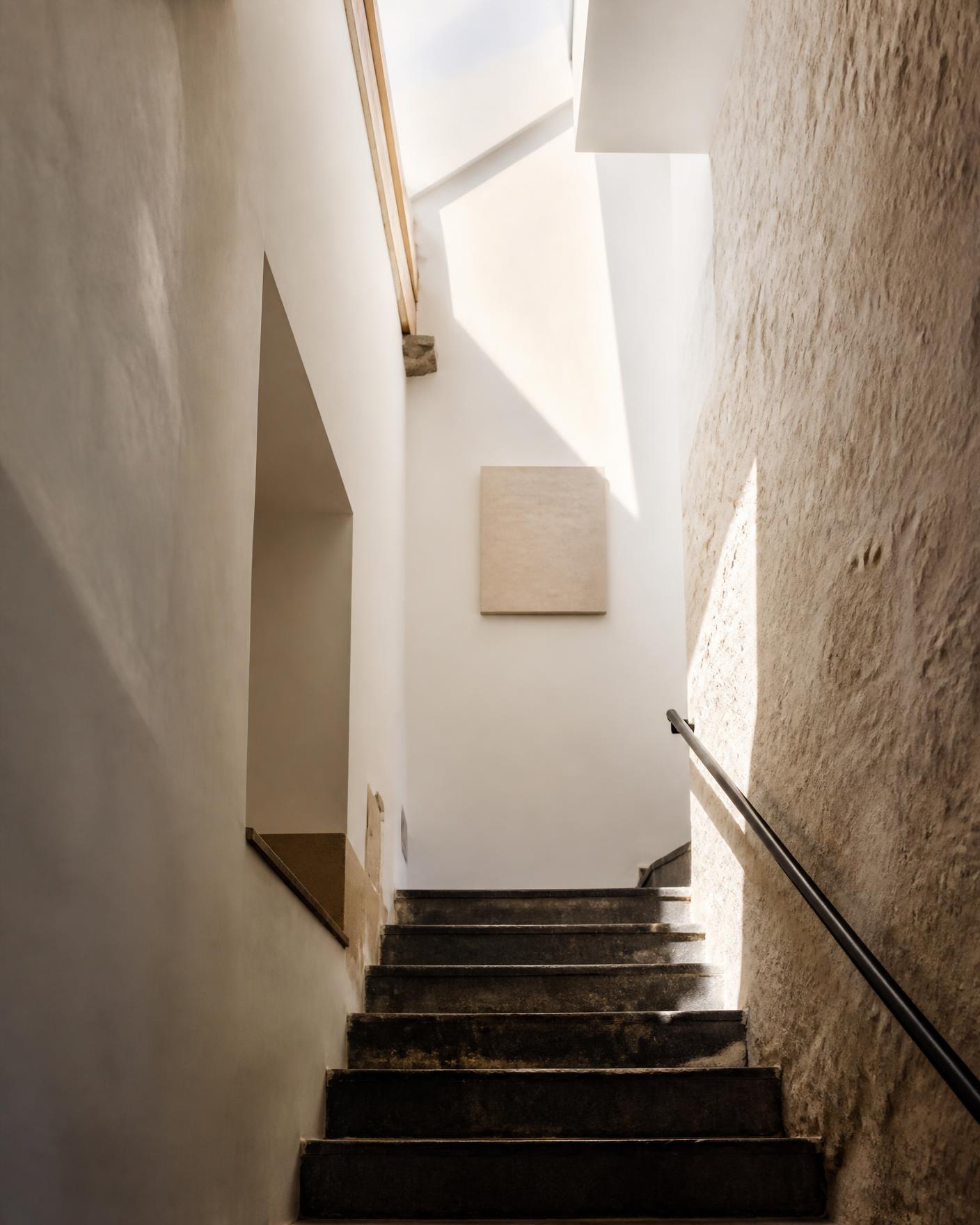 Escadaria interior em pedra com paredes de cal e luz zenital, Alfama